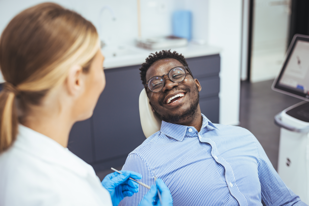 A dentist is speaking with a smiling patient seated in a dental chair during a routine dental examination or consultation.