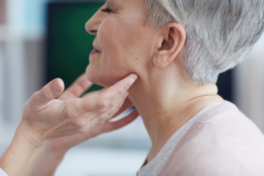Dentist gently examining an older woman's neck and jaw during an oral health consultation to check for swelling or other dental-related conditions.