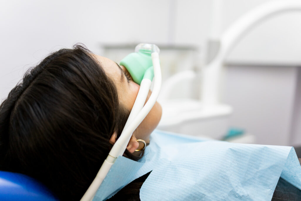 A patient reclines in a dental chair wearing a nasal mask to receive nitrous oxide sedation before or during a dental procedure.